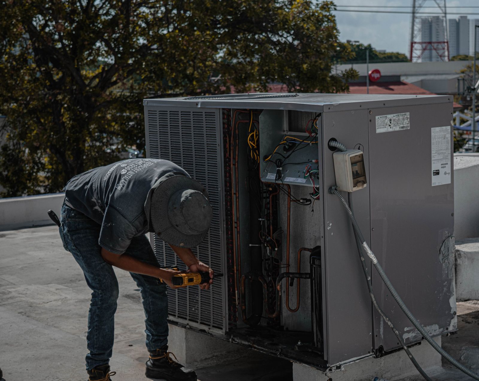 Technician repairing a rooftop air conditioning condenser unit with hand tools